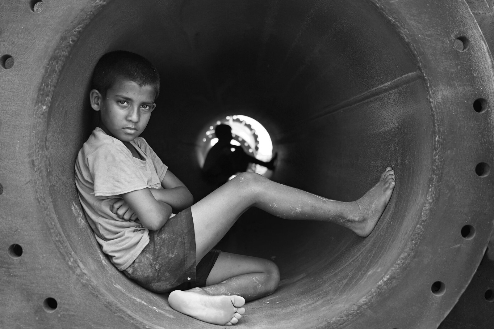 Grayscale Photo of Boy in Crew Neck T-Shirt Sitting in Round Pipe